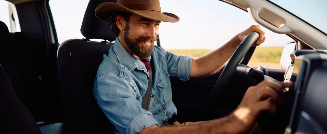 Homem com chapéu selecionando uma música no rádio do carro