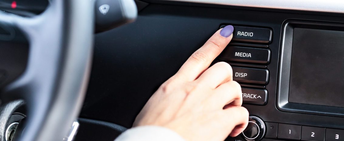 Mulher pressionando o botão de ligar do rádio de um carro.