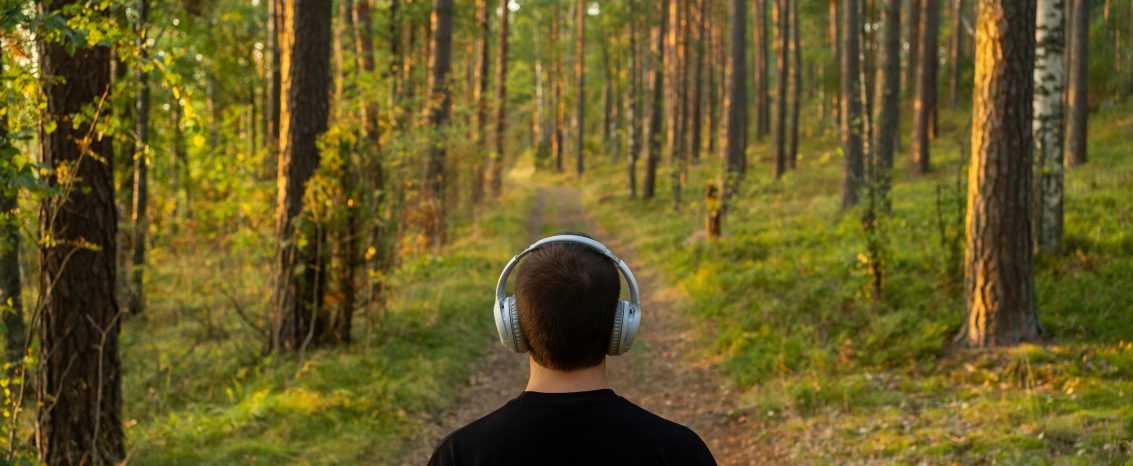 Homem com camiseta preta escutando áudio em meio a natureza